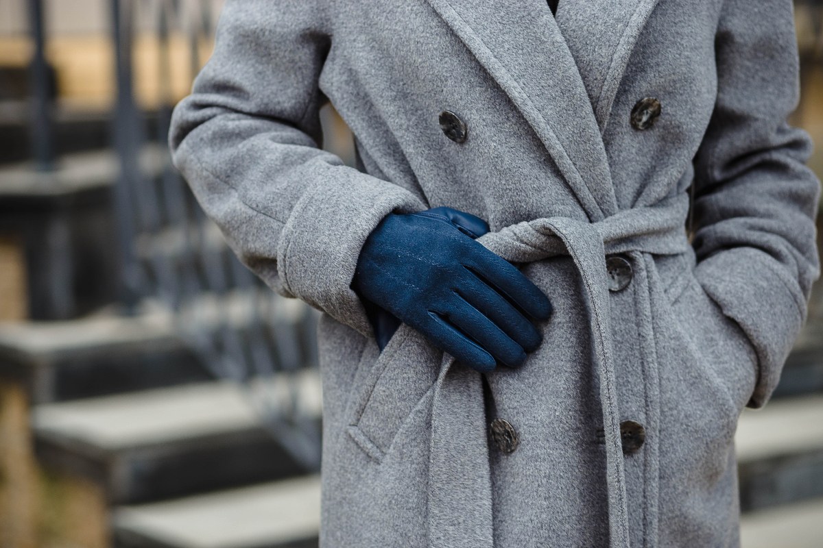Dettaglio di cappotto invernale grigio con guanto blu