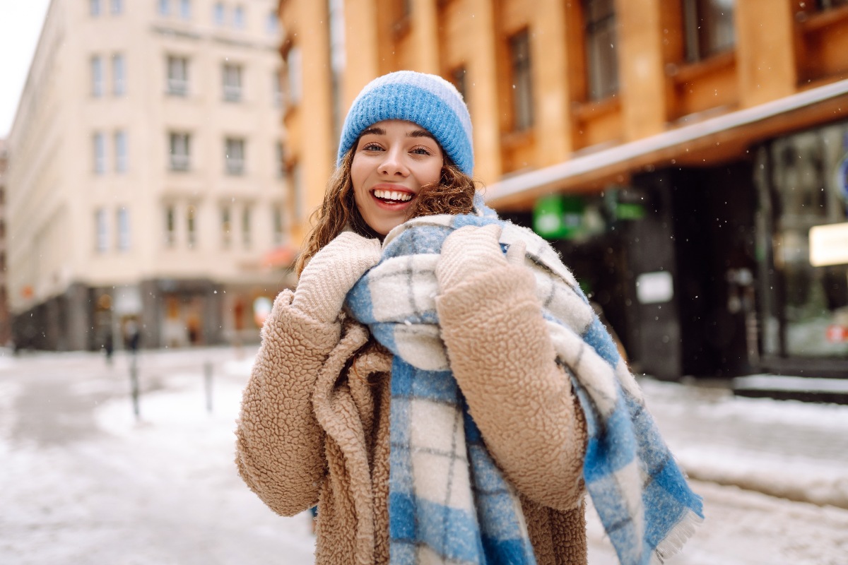 Ragazza sorridente avvolta in un cappotto teddy con sciarpa e cappello sulla neve
