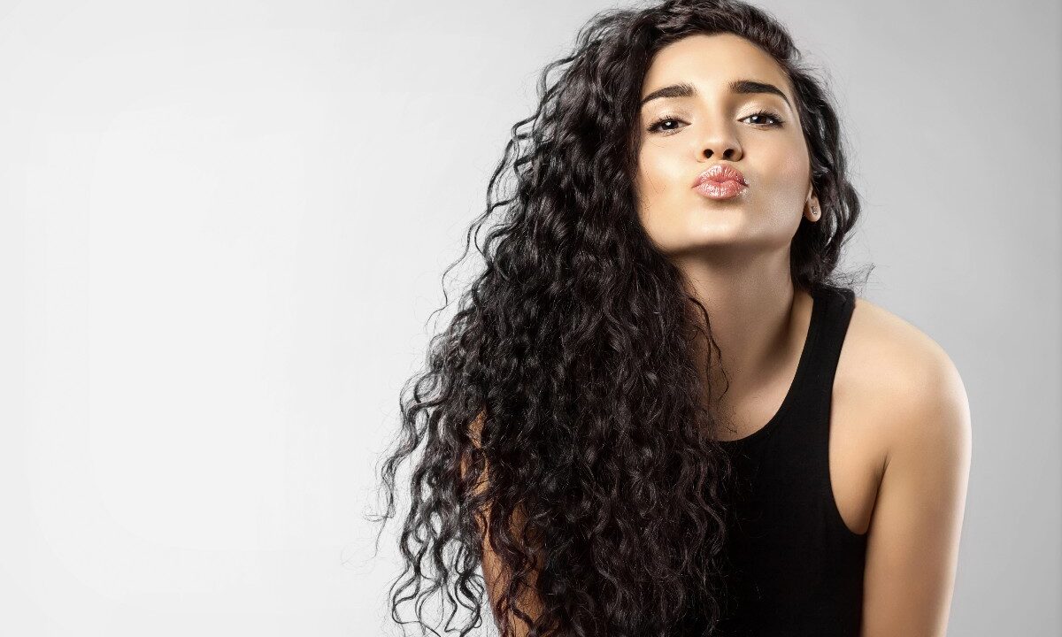 Giovane donna con folti capelli neri e ricci ritratta mentre manda un bacio.