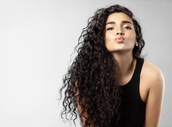 Giovane donna con folti capelli neri e ricci ritratta mentre manda un bacio.
