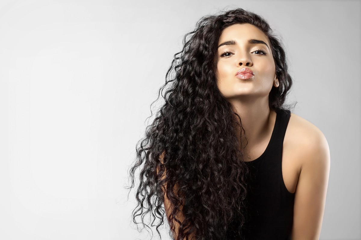 Giovane donna con folti capelli neri e ricci ritratta mentre manda un bacio.